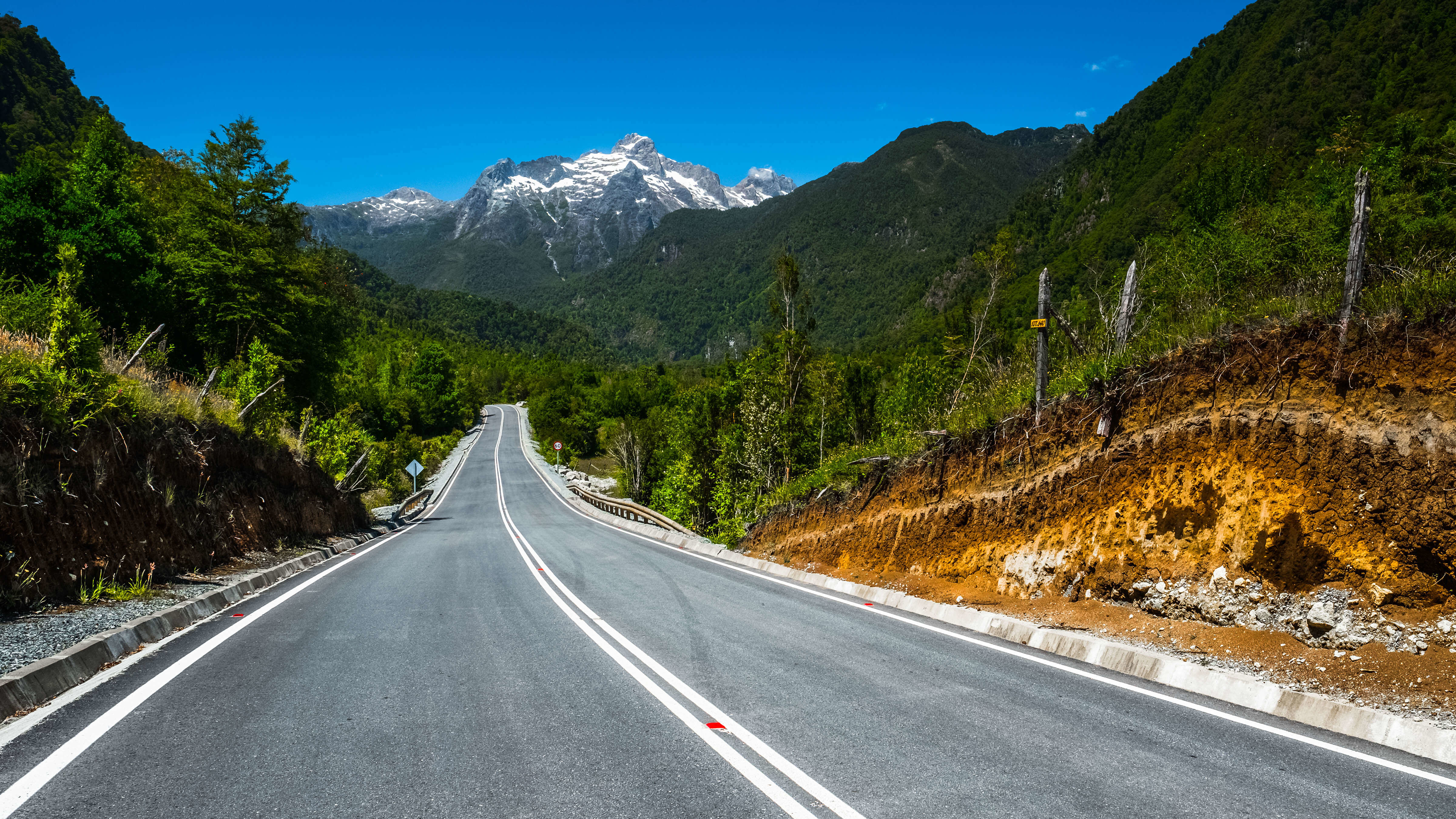 Tramo pavimentado de la Carretera Austral con los picos nevados de la Cordillera de los Andes de fondo